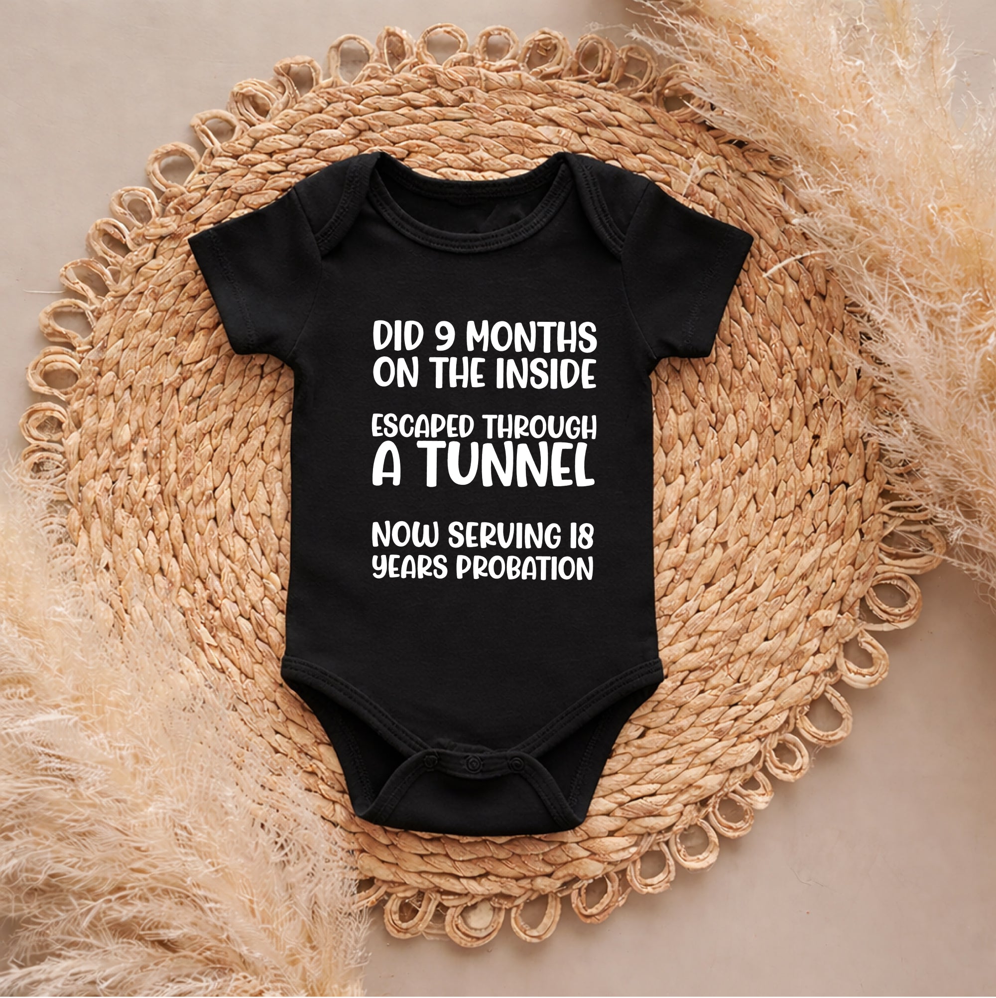 Black baby onesie with humorous text on a woven mat