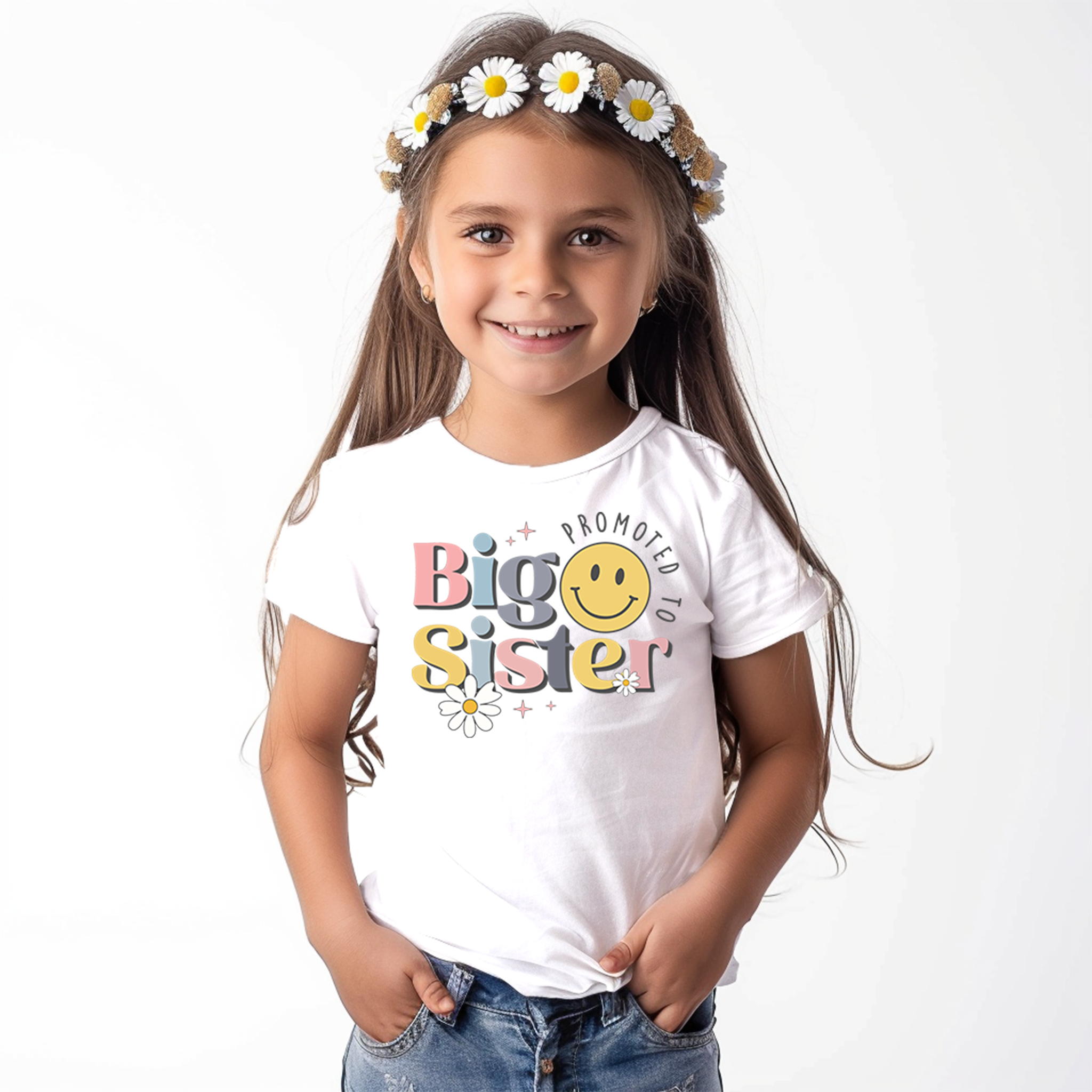 A young girl is posing with a proud smile, wearing a white Trendy Tykes T-shirt that reads "Big Sister" in colorful, playful letters, embellished with a smiling sun, stars, and flowers, which emphasize the joy of being promoted to a big sister.