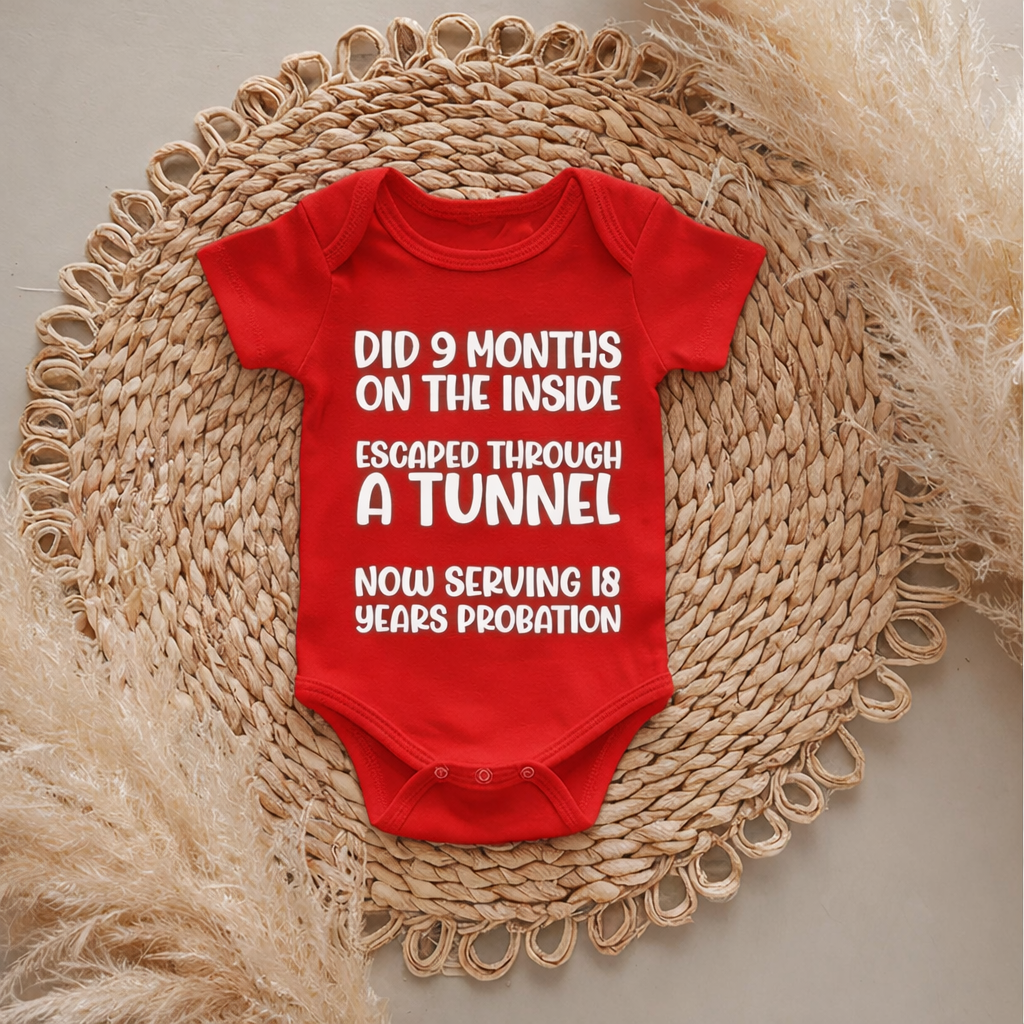 Red baby onesie with humorous text on a woven mat