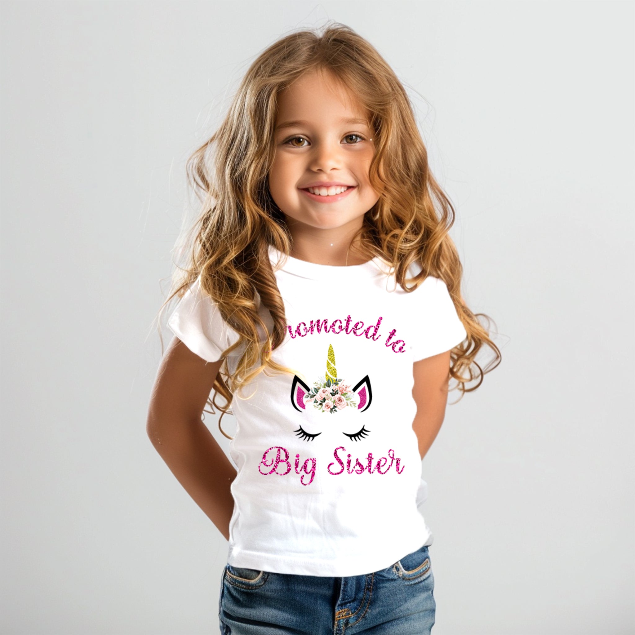 A joyful child wearing a Trendy Tykes brand white T-shirt with "Promoted to Big Sister" and a glittery unicorn graphic