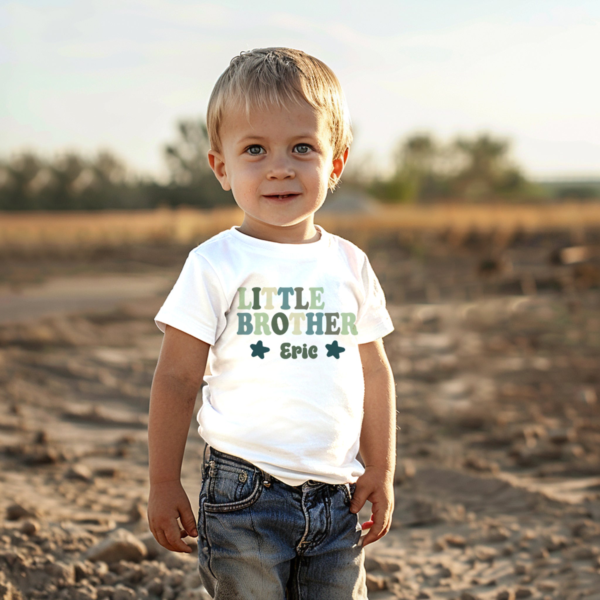 personalized white t-shirt by Trendy Tykes with the words "LITTLE BROTHER" above his name personalised name, both printed in varying shades of green. The design includes decorative stars, emphasizing the proud title of being a little brother.